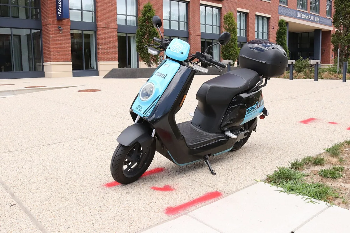 Zwart-blauwe deelscooter geparkeerd op straat bij een gebouw