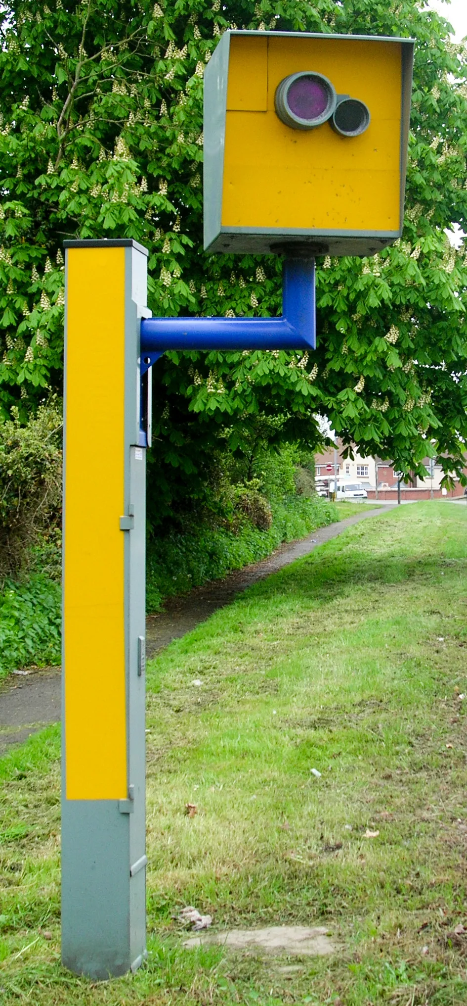 Gele flitspaal langs de weg met groene begroeiing op de achtergrond