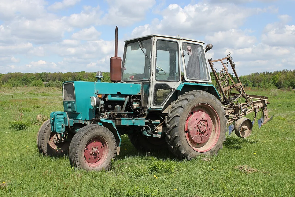 Landbouwtractor met ploeg op een grasveld tegen een bewolkte lucht