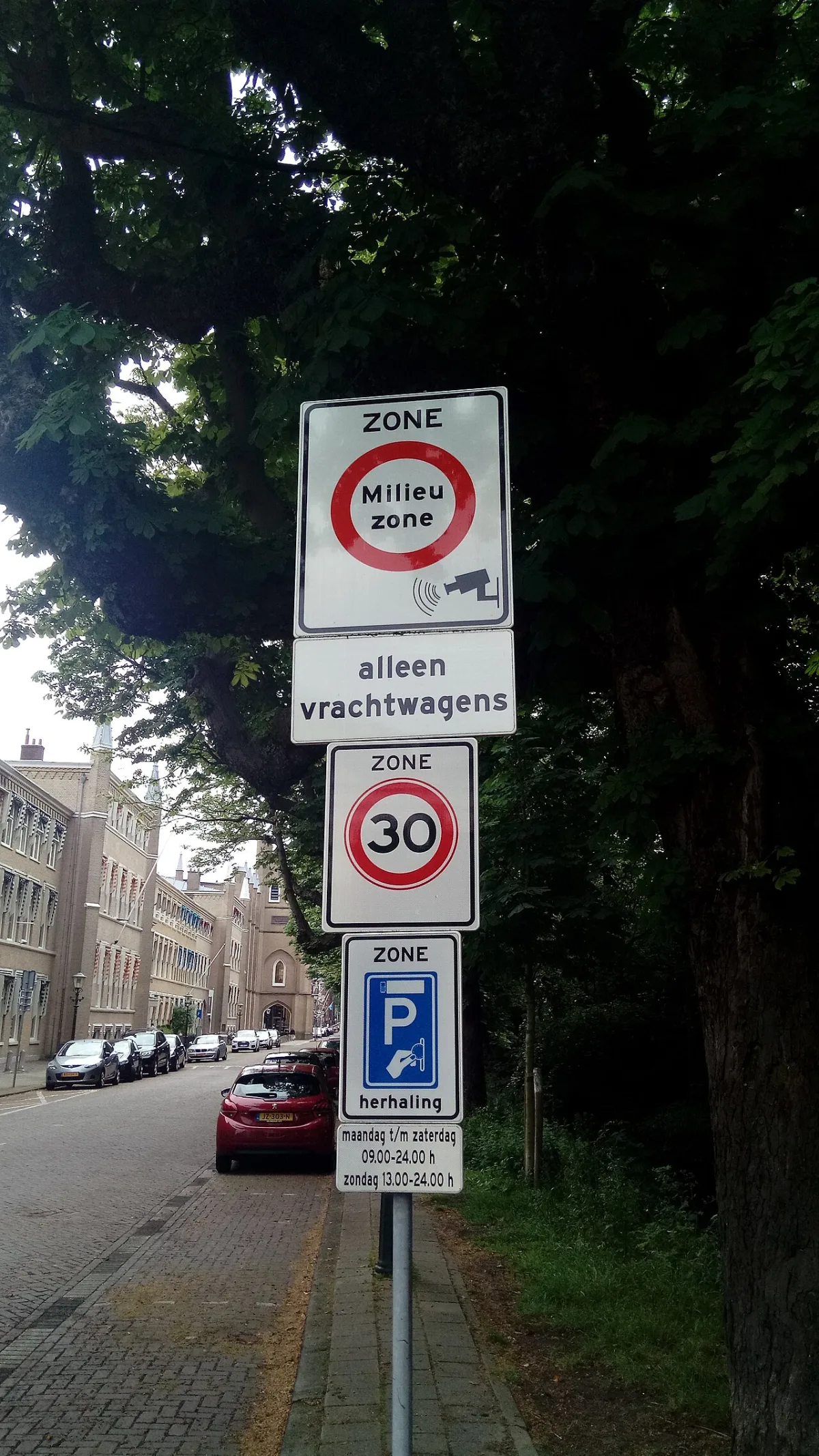 Verkeersborden op een paal in Den Haag met een milieuzone, een 30 km/u-zone en een parkeerzone langs een straat met geparkeerde auto's.